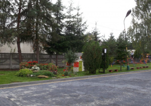 Ogród przedszkolny przedstawiający skalniak, drzewa oraz częściowo plac zabaw